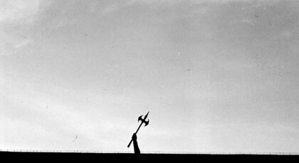 Silhouette of a hand holding a medieval battle axe against a dramatic sky.