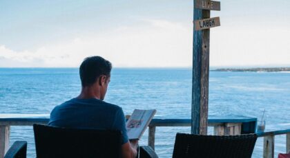 A man relaxes with a book overlooking the ocean in Bali, enjoying leisure time.