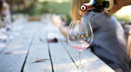 A hand pouring red wine into a glass on an outdoor table, creating a relaxed atmosphere.