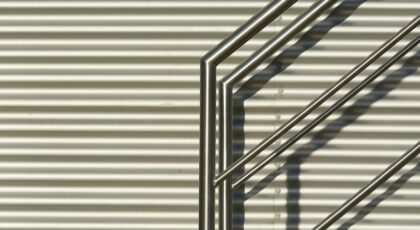 Close-up of sleek metal railings casting shadows on a corrugated wall with industrial design.