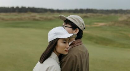 A young couple in casual attire embracing on a serene outdoor golf course.