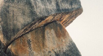 A man meditates peacefully beside massive boulders on a serene seashore.