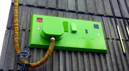 Low-angle view of a green electric outlet on a textured building wall.