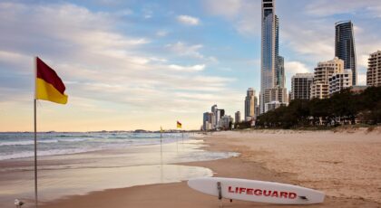 Capture of Surfers Paradise beach with skyline at sunset, lifeguard board and flags visible.