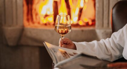 Woman relaxing by the fireplace with a book and wine, creating a warm ambiance.