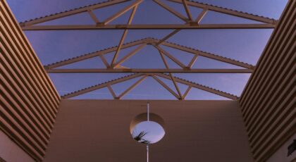 From below of contemporary building with ribbed walls and creative geometric construction on roof against purple sunset sky