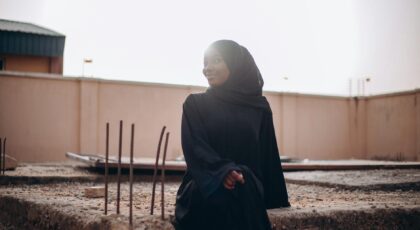 A young woman in a black hijab sits at a construction site during sunset, exuding a serene mood.