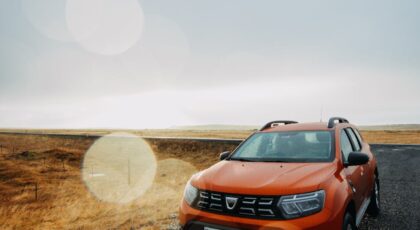 Orange Dacia Duster SUV on a wet rural road under a cloudy sky.