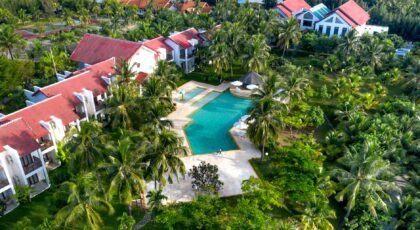 Aerial view of a luxury resort featuring a swimming pool, villas, and lush palm trees.