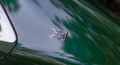 Close-up of a Union Jack emblem on a sleek green luxury car hood, highlighting automotive elegance.