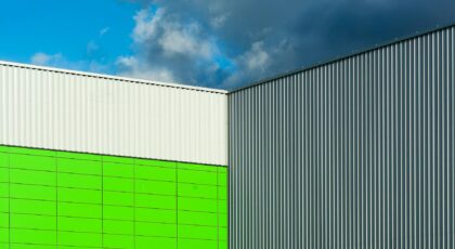 Close-up of a modern building facade with colorful panels and corrugated metal against a dramatic blue sky.