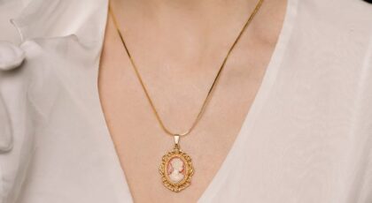 Portrait of a stylish woman wearing an elegant gold cameo necklace and white blouse, capturing vintage elegance.