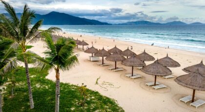 Picturesque tropical beach with palm trees and umbrella huts on a cloudy day.