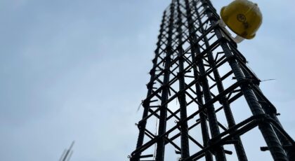 Vertical steel reinforcement bars on site with hanging helmet indicating construction safety focus.