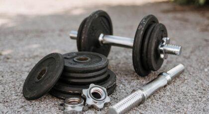 Heavy adjustable dumbbell near cast iron plates and hexagonal collars with stainless steel bar on pavement