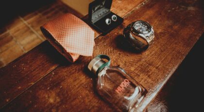 From above composition of silk tie above male perfume bottle and steel watch with cufflinks located on dark wooden surface