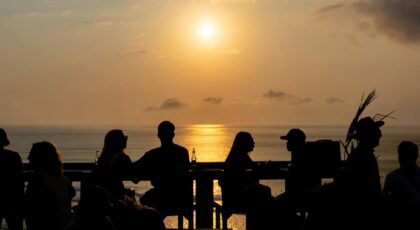 Silhouettes of people enjoying a Bali sunset at a beachside bar, perfect vacation vibe.