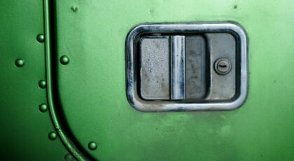 Detailed close-up of a metallic door handle with keyhole on green metal surface.