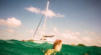 A person floating in turquoise water near a sailboat under a sunny sky.