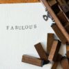 Close-up of wooden letter stamps with 'Fabulous' text on paper, artistic flatlay.