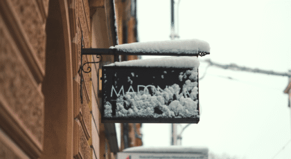 A snow-covered sign along a historic street in Krakow, Poland, during winter.
