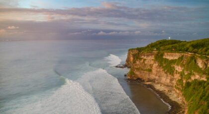 Breathtaking aerial view of Uluwatu cliffs in Bali with vibrant ocean waves during sunset.