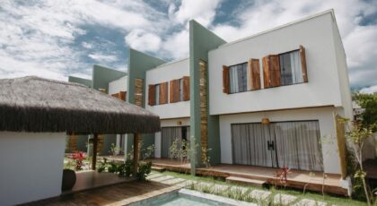 Stylish modern villas with wooden accents and thatched roofing by a pool under a vibrant sky in Bahia, Brazil.